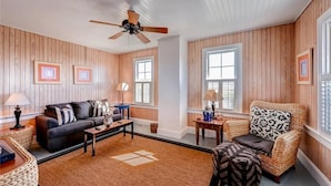A living room with a sofa, armchairs, a coffee table, and a ceiling fan.