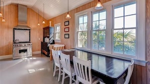A kitchen with wooden walls, a stove, a dining table with chairs, and large windows.