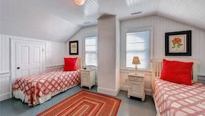 A bedroom with two beds, a window with blinds, a red rug, and a ceiling light fixture.