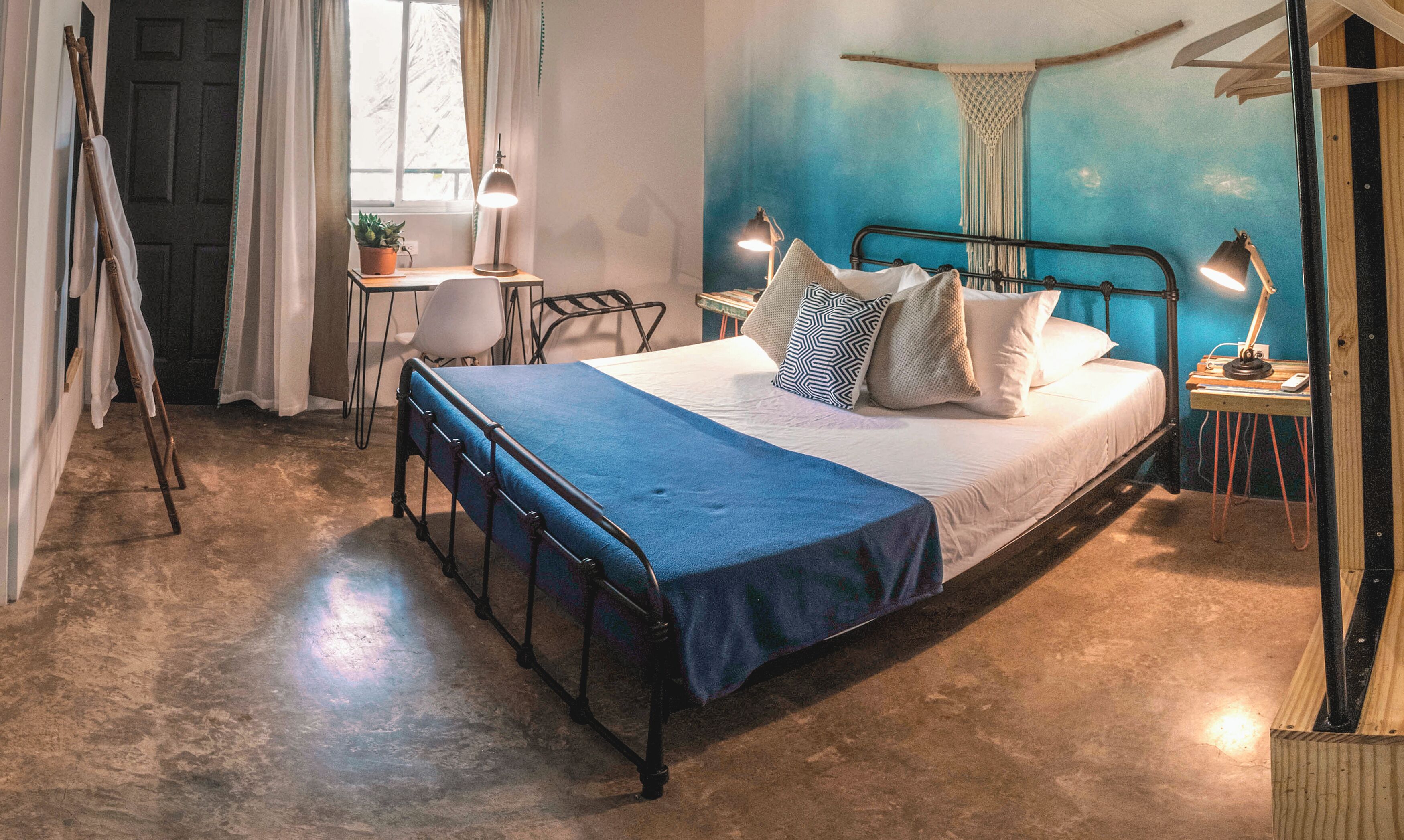 Een slaapkamer met een metalen bedframe, een blauw sprei en twee bedlampjes.