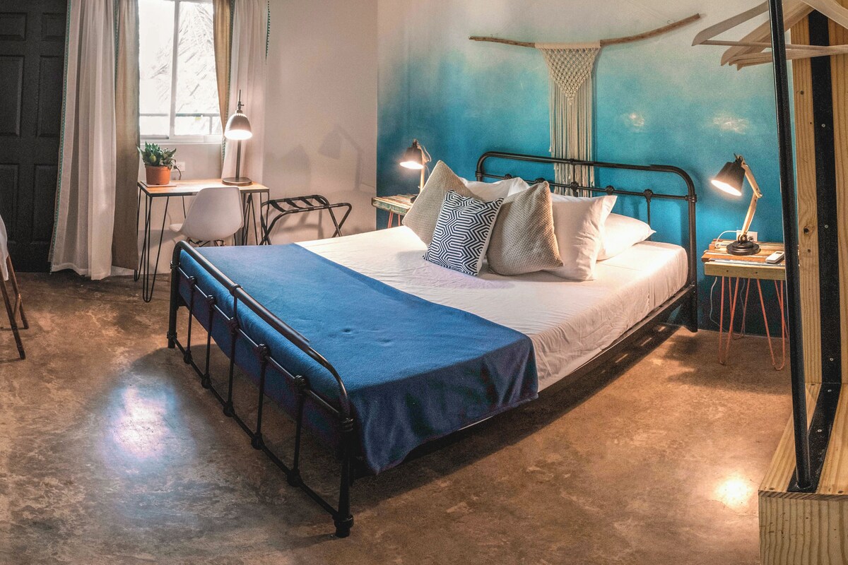 A bedroom with a metal bed frame, a blue bedspread, and two bedside lamps.