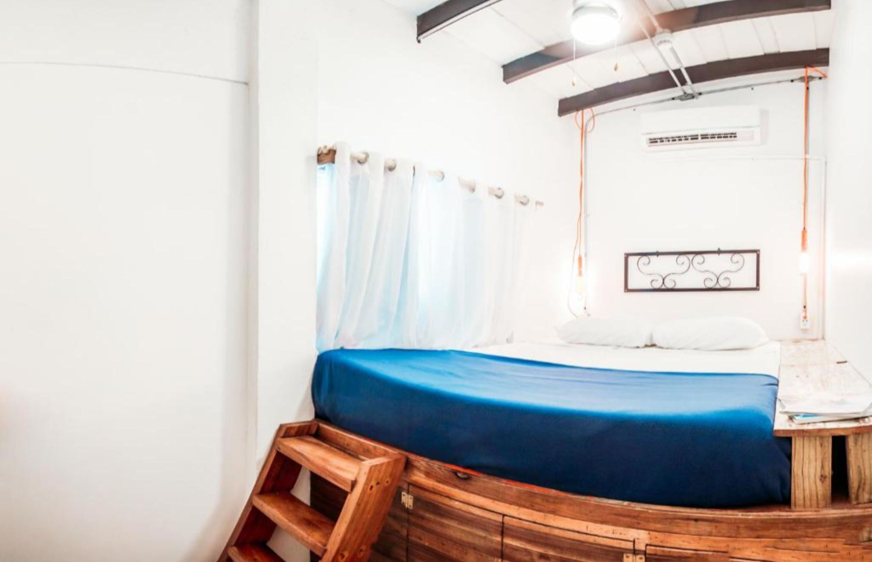 Een kamer met een bed, een houten bankje, een witte muur, een plafondlamp en een decoratief metalen object.