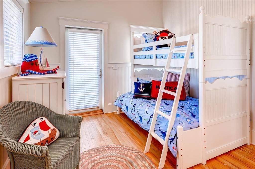 Een kinderkamer met een stapelbed, een stoel, een lamp en een raam met jaloezieën.