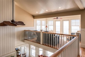 A spacious upper floor with a wooden railing, large windows, and a ceiling fan.