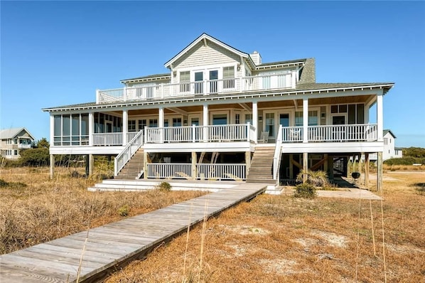 A two-story beach house with a wooden deck and a staircase leading to the upper level.
