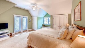A bedroom with a large bed, a ceiling fan, and a television on a stand.