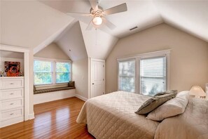 Une chambre avec un grand lit, un ventilateur de plafond et une fenêtre avec des stores.