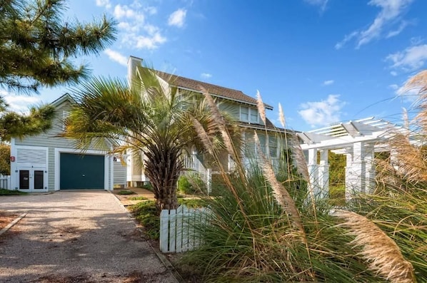A two-story house with a garage, surrounded by tropical vegetation.