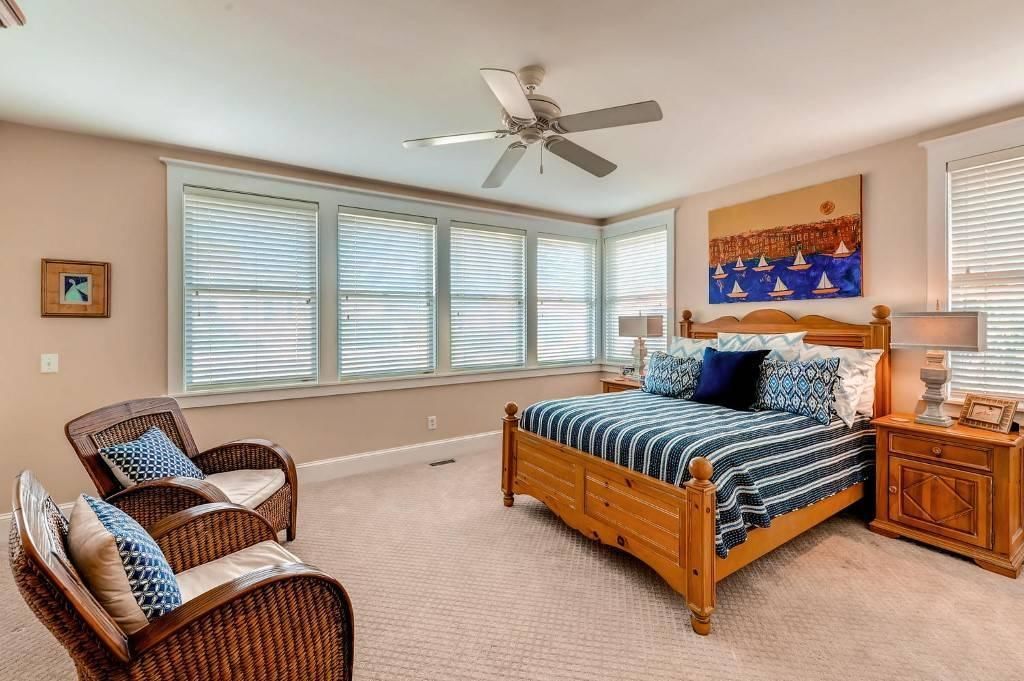 A bedroom with a bed, two wicker chairs, a ceiling fan, and a painting on the wall.