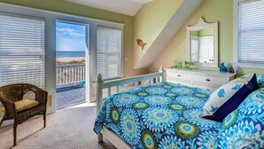 A bedroom with a bed, a chair, a dresser, and a balcony with a view of the beach. - Footprints In The Sand 4 Bedroom Holiday Home By Bald Head Island (Bald Head Island)