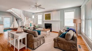 A spacious living room with a staircase, a fireplace, and a ceiling fan. - Footprints In The Sand 4 Bedroom Holiday Home By Bald Head Island (Bald Head Island)