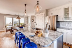 A modern kitchen with a marble countertop, stainless steel appliances, and blue bar stools.