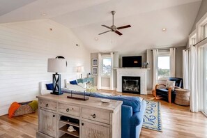 A spacious living room with a fireplace, a ceiling fan, and a television. - Hat Trick 4 Bedroom Holiday Home By Bald Head Island (Bald Head Island)