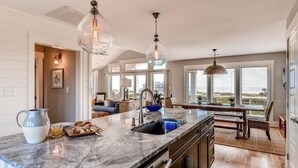 A kitchen with a marble countertop, a sink, and a dining area with a bench. - Hat Trick 4 Bedroom Holiday Home By Bald Head Island (Bald Head Island)