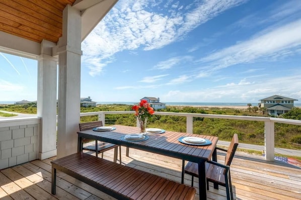 A wooden deck with a table set for two, overlooking a beach and ocean.
