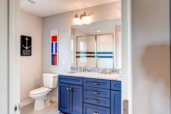 Un baño moderno con inodoro blanco, muebles azules y un espejo grande.