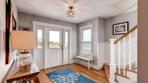 A hallway with a wooden floor, a blue rug with fish patterns, a lamp, a jar of snacks, and a staircase with white railings. - Hat Trick 4 Bedroom Holiday Home By Bald Head Island (Bald Head Island)