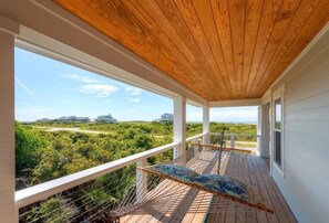 Una terraza de madera con una hamaca y vistas al paisaje costero.