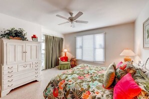A bedroom with a floral bedspread, a white dresser, a ceiling fan, and a window with blinds. - Indigo Pelican Indigo Pelican 5 Bedroom Holiday Home By Bald Head Island (Bald Head Island)