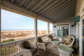 Une véranda aménagée avec des meubles en osier, une table en verre et une vue sur la plage.