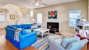A living room with a blue sofa, patterned armchairs, a white coffee table, a fireplace, and a staircase.
