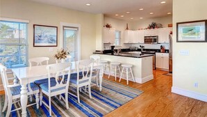A modern kitchen with white cabinets, a central island, and a dining area with white chairs and a striped rug.