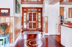 Un pasillo con puertas de madera, una zona de cocina con armarios y una mesa de comedor.