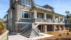 A two-story house with a covered porch, a staircase leading to the entrance, and a landscaped yard. - Island Belle 4 Bedroom Holiday Home By Bald Head Island (Bald Head Island)