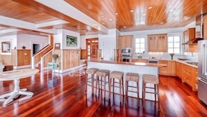 A spacious kitchen with wooden flooring, a central island with bar stools, and modern appliances. - Island Belle 4 Bedroom Holiday Home By Bald Head Island (Bald Head Island)