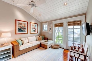 A cozy living room with a sofa, a coffee table, and a TV mounted on the wall. There are framed pictures on the wall and a ceiling fan. - Island Belle 4 Bedroom Holiday Home By Bald Head Island (Bald Head Island)