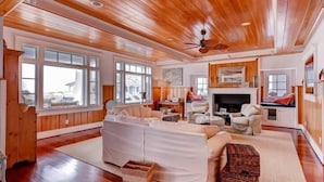A spacious living room with wooden ceilings and large windows, a fireplace, and a television. - Island Belle 4 Bedroom Holiday Home By Bald Head Island (Bald Head Island)