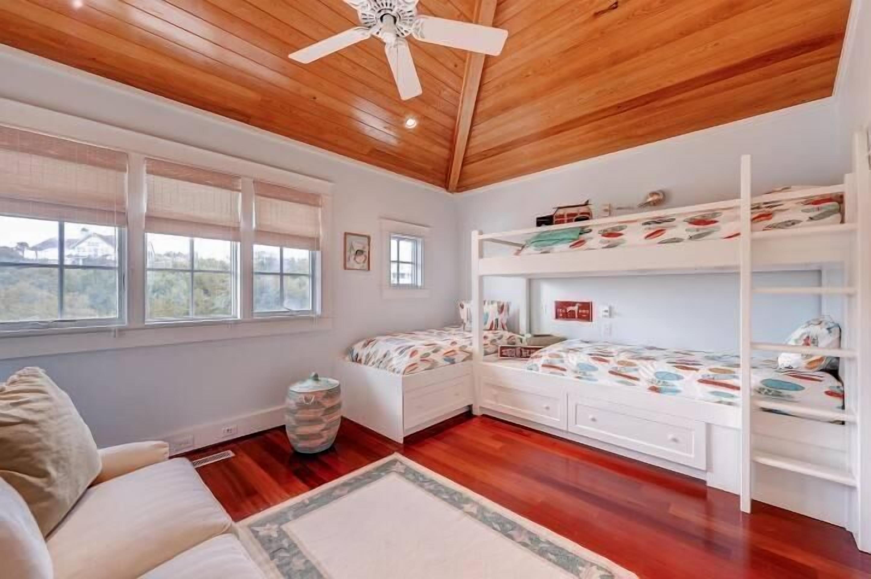 Un dormitorio con techo de madera, literas, un aparador blanco y una ventana con vistas.