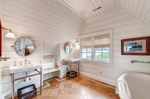 Un baño con paredes de madera blanca, dos lavamanos, una bañera y un espejo grande.