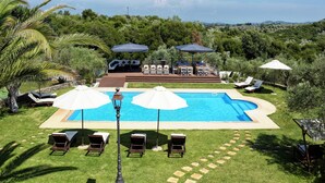 Une piscine entourée de verdure, agrémentée de chaises longues et de parasols, ainsi qu’une terrasse avec des espaces pour s’asseoir.
