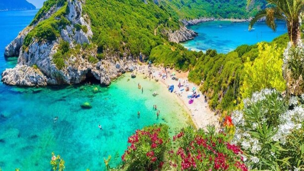 Un paysage côtier avec une plage, des eaux turquoise et limpides, et des collines verdoyantes.