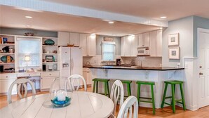 A modern kitchen with white cabinets, a black countertop, and green bar stools. - Island Retreat 4 Bedroom Holiday Home By Bald Head Island (Bald Head Island)