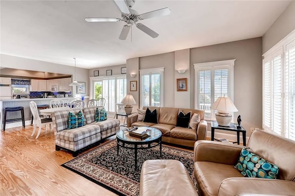 A spacious living room with a sofa, armchairs, and a coffee table. There is a dining area with a table and chairs, and a kitchen in the background.
