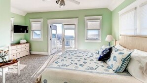 A bedroom with a bed, a dresser, a television, and a balcony. - JJ s Hideaway 4 Bedroom Holiday Home By Bald Head Island (Bald Head Island)