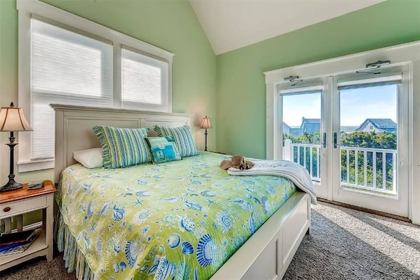 A bedroom with a bed, two bedside lamps, a nightstand, and a view of the outside through a sliding glass door.