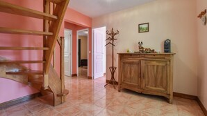 Ein geräumiges Zimmer mit einer Holztreppe, Fliesenboden, einem Holzschrank und einem Kleiderständer.