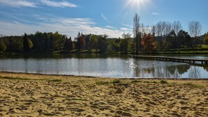 Ein Sandstrand mit einem ruhigen See, einer Holzsteg und Bäume im Hintergrund.
