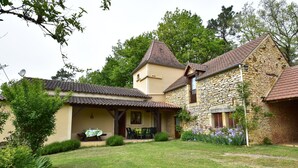 Ein zweistöckiges Haus mit Steinaußenwand und Ziegeldach, mit überdachter Terrasse und Gartenmöbeln.