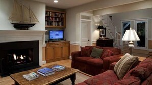 A living room with a fireplace, a television, a bookshelf, a red sofa, and a lamp. - Kate s Choice 5 Bedroom Holiday Home By Bald Head Island (Bald Head Island)