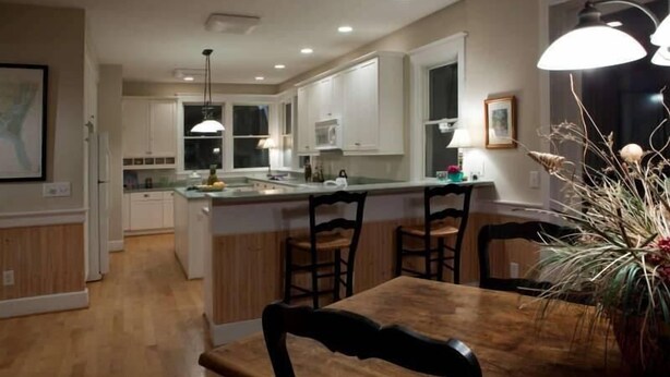 A modern kitchen with white cabinets, a wooden dining table, and pendant lighting. - Kate s Choice 5 Bedroom Holiday Home By Bald Head Island (Bald Head Island)