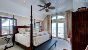 A four-poster bed with a bench, a ceiling fan, and a view of the ocean through large windows. - Loggerhead Lady 4 Bedroom Holiday Home By Bald Head Island (Bald Head Island)