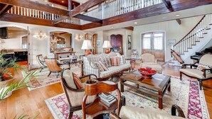 A spacious living room with a high ceiling, wooden beams, a staircase, and a cozy seating area with a sofa and armchairs. - Loggerhead Lady 4 Bedroom Holiday Home By Bald Head Island (Bald Head Island)