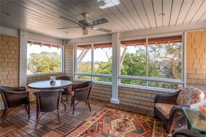 A sunroom with a brick wall, large windows, wicker furniture, and a ceiling fan. - Marsh Madness 7 Bedroom Holiday Home By Bald Head Island (Bald Head Island)