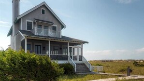 A two-story house with a porch, a chimney, and a view of the beach. - Paradise 3 Bedroom Holiday Home By Bald Head Island (Bald Head Island)