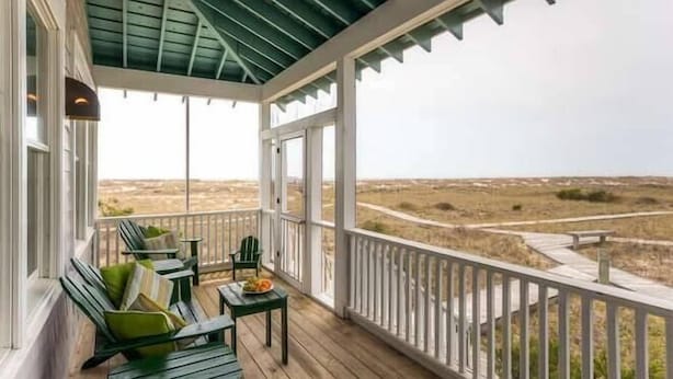 A covered porch with wooden flooring, green chairs, and a table with a plate of fruit. - Paradise 3 Bedroom Holiday Home By Bald Head Island (Bald Head Island)