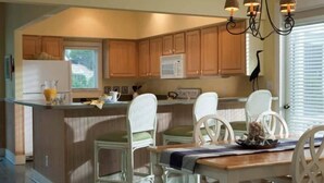 A kitchen with wooden cabinets, a central island with seating, a microwave, and a chandelier. - Purrfect Paws 2 Bedroom Holiday Home By Bald Head Island (Bald Head Island)
